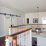In this upstairs hallway, you can see a handrail built in the traditional New England style. Note also the sliding barn-style doors with exposed runner and powder bathroom. The bathroom has a cute bit of personalization—the glass in the wood door has the letters WC etched into it (for water closet of course!)